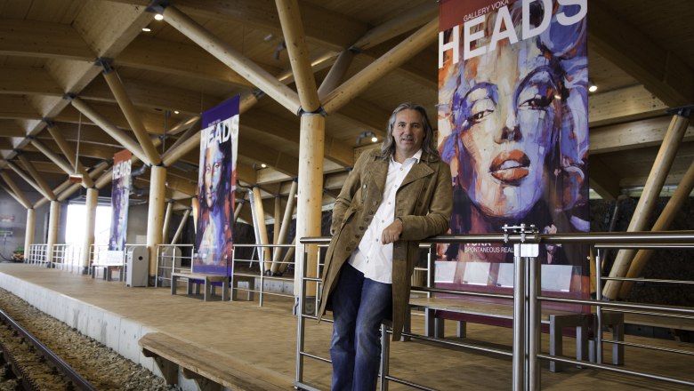 A man stands in a modern train station next to art posters with portraits.