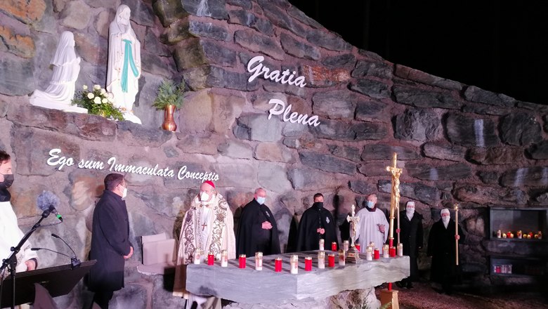 Priest in a grotto with statues and candles.