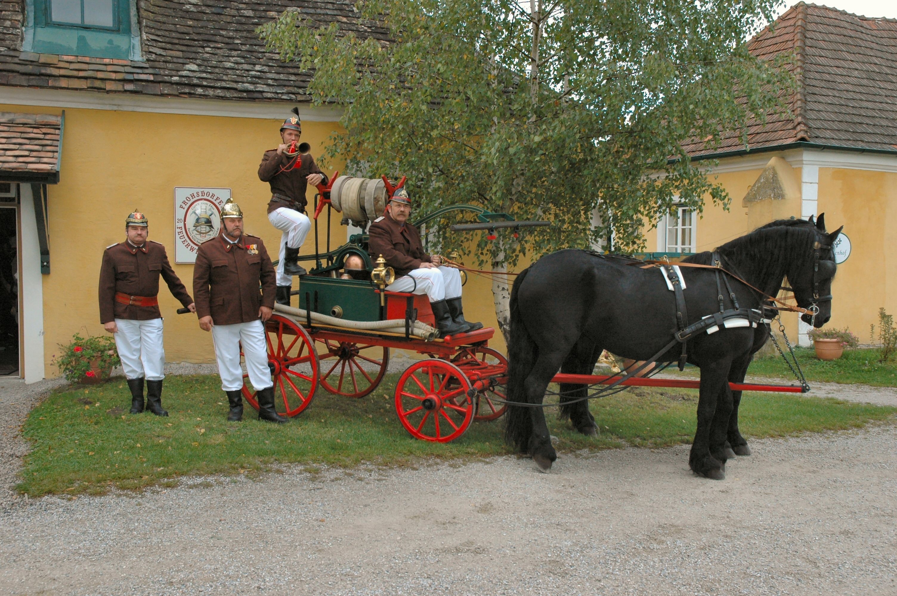 Historic fire engine with horse and firemen in uniform in front of a yellow building.