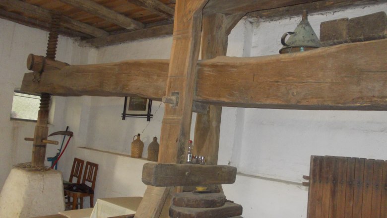 Old wine press in a rustic room with wooden beams and antique objects.