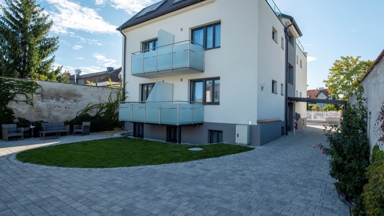 Modern three-story building with balconies and paved courtyard.