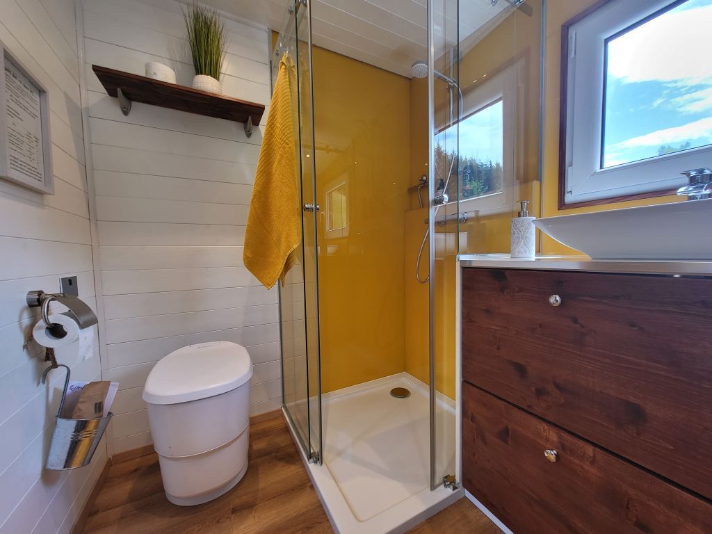Modern bathroom with yellow shower screen, white WC, wooden shelf and window.