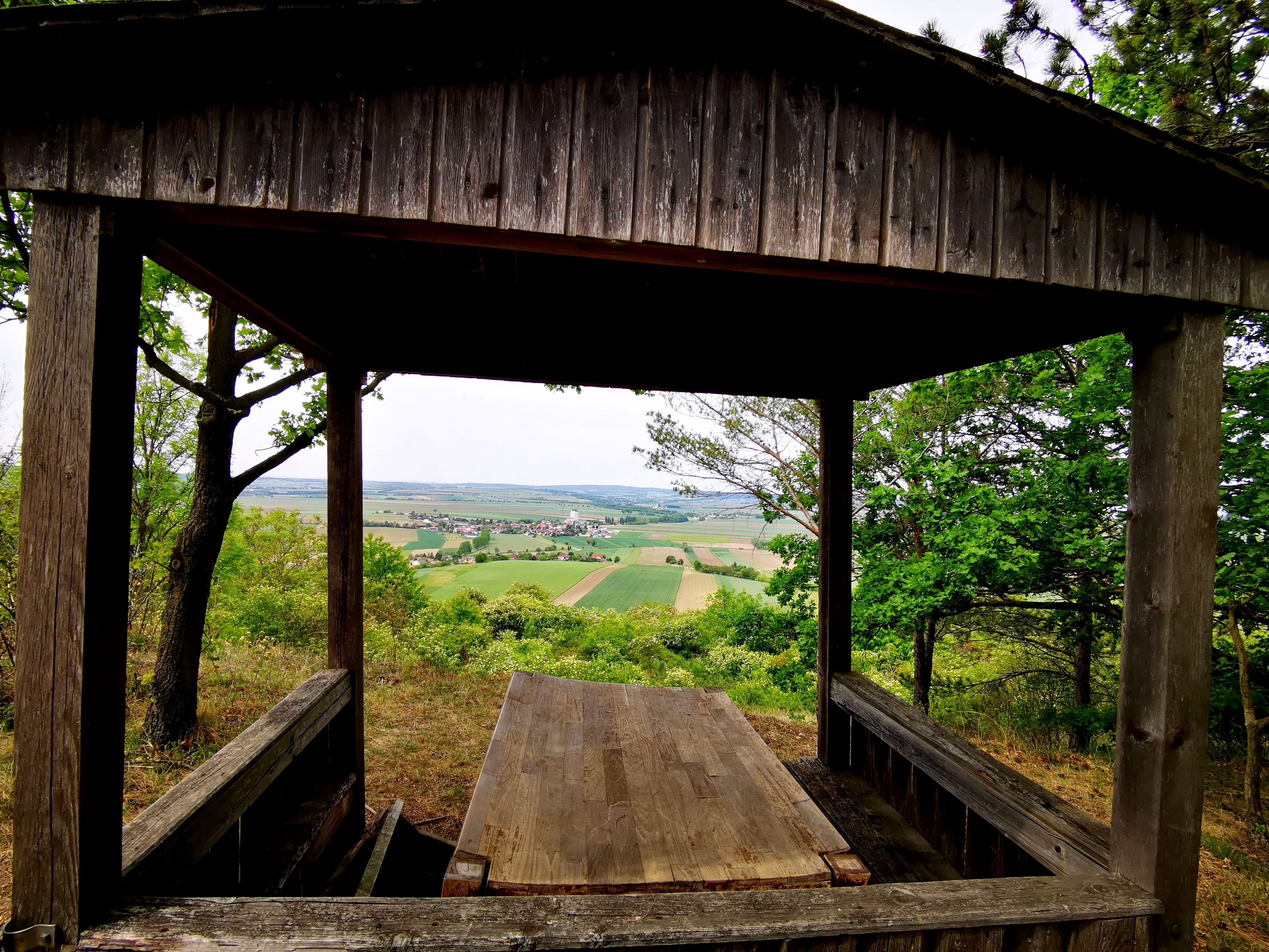 Wooden hut with view of fields and village in the distance.
