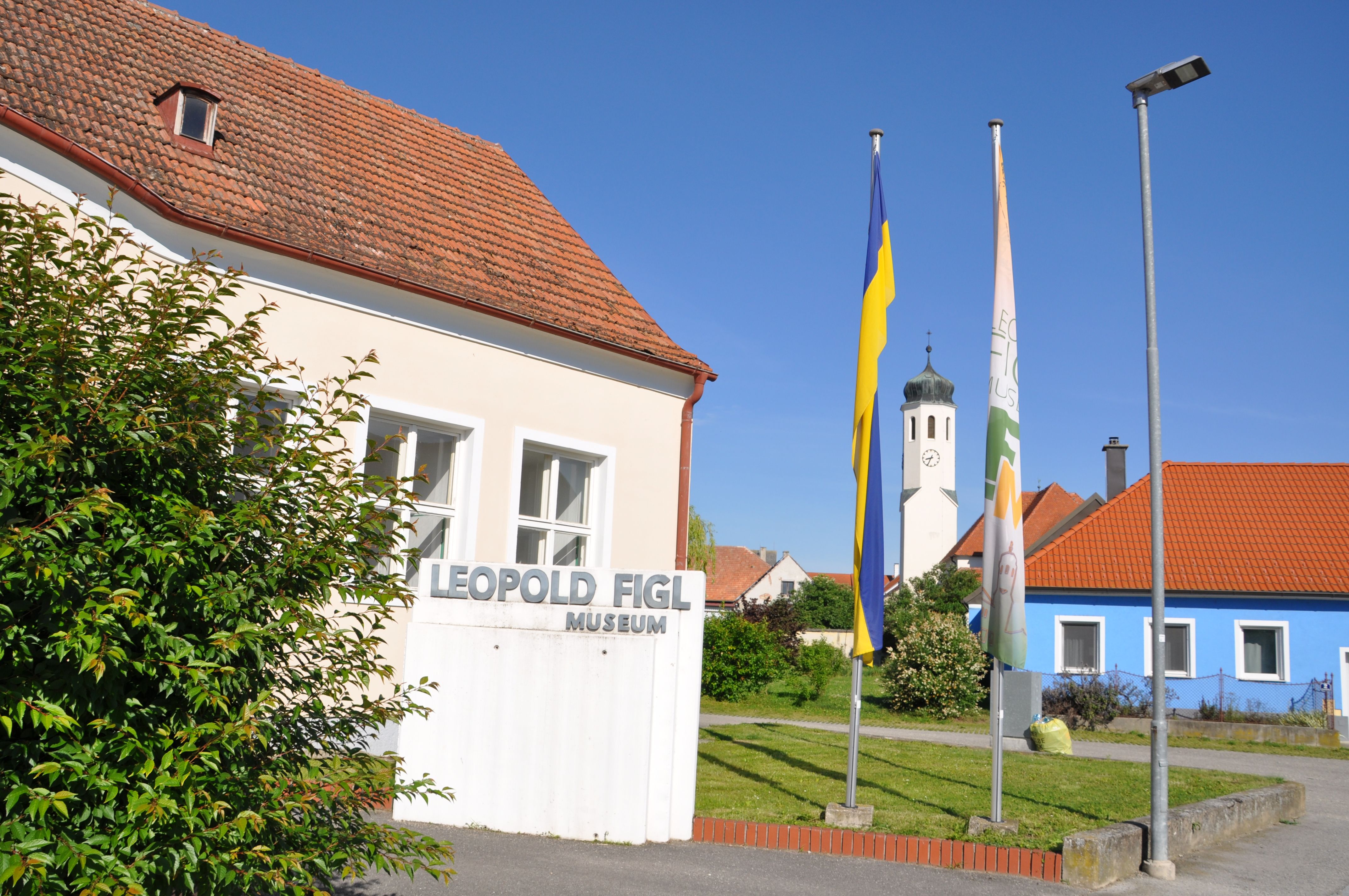 Leopold Figl Museum with flags and church tower in the background.