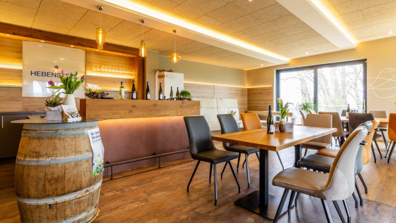 Modern tasting room with wooden tables, chairs and a bar. Wine bottles and flowers decorate the room.