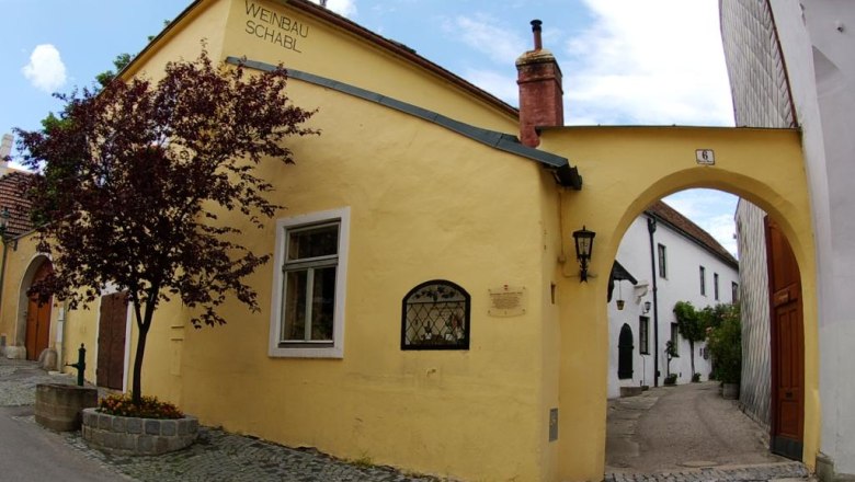 Yellow building with the inscription 'Weinbau Schabl', next to it an archway and a tree.