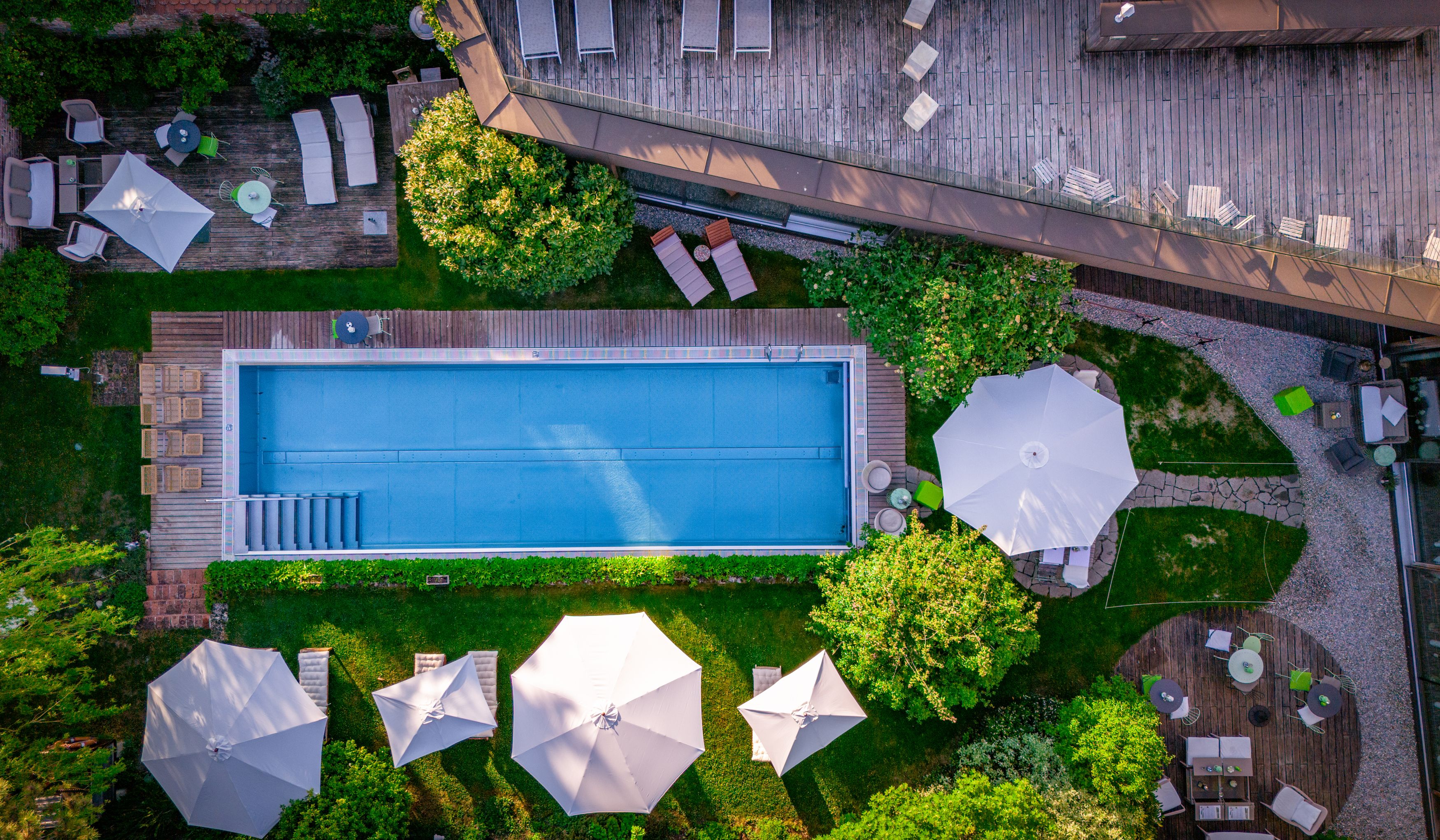 Aerial view of a pool with surrounding sun loungers and parasols in a garden.