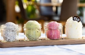 Four glasses with different types of ice cream on a wooden board.