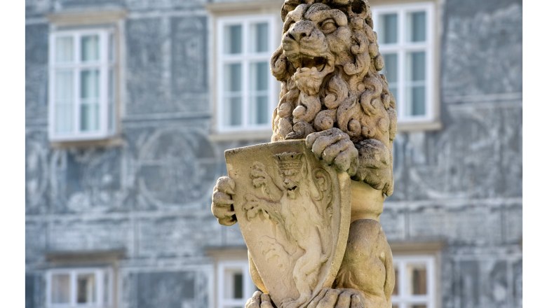 Stone lion with coat of arms on a fountain in front of a building.