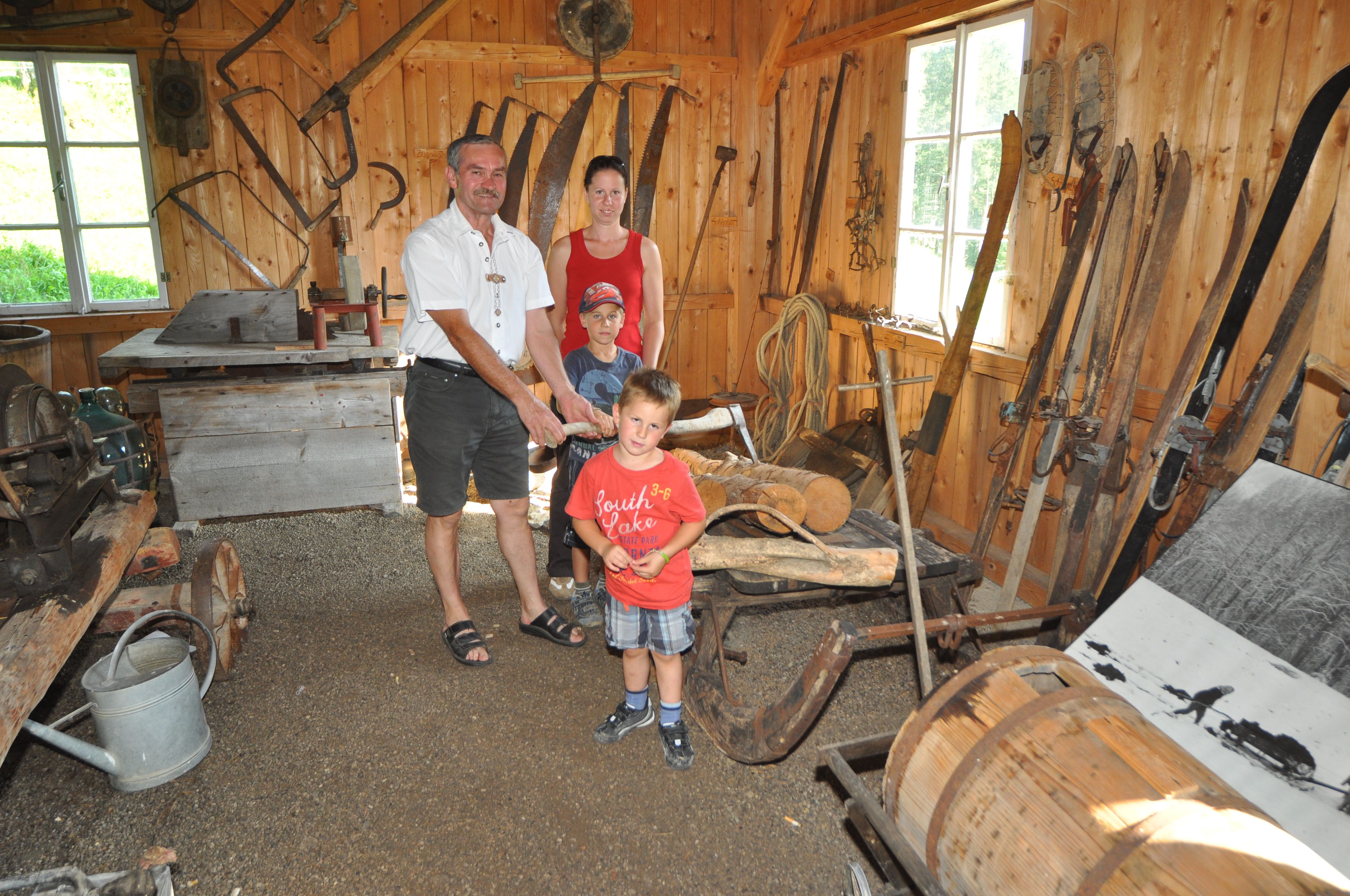 A family in a rustic room with old farming tools and equipment.