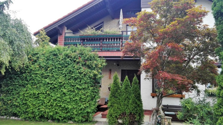 Exterior view of a house with balcony, surrounded by trees and bushes.