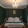 Elegant hotel room with green decor, double bed, chandelier and curtains.