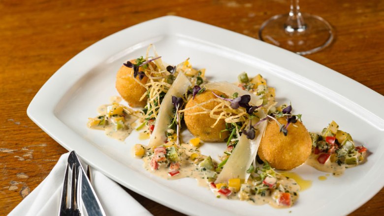 Three golden-brown croquettes on a white plate, garnished with vegetables and sauce.
