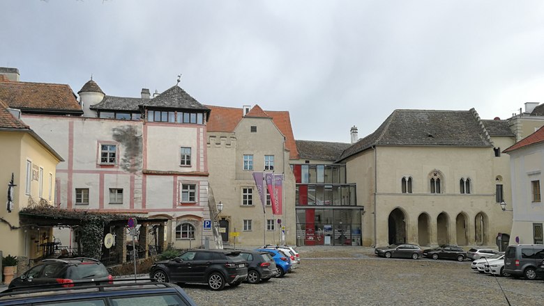 Historic buildings on Hoher Markt with parked cars on cobblestones.