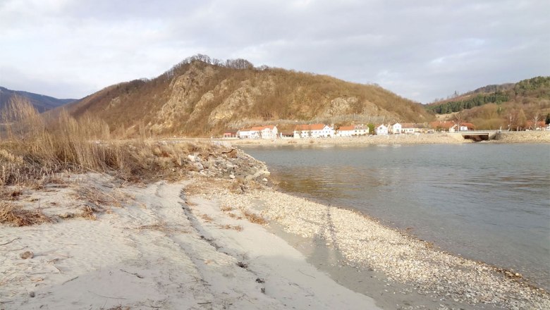 beach, © Kowalski A quiet beach with pebbles, a village and wooded hills in the background.