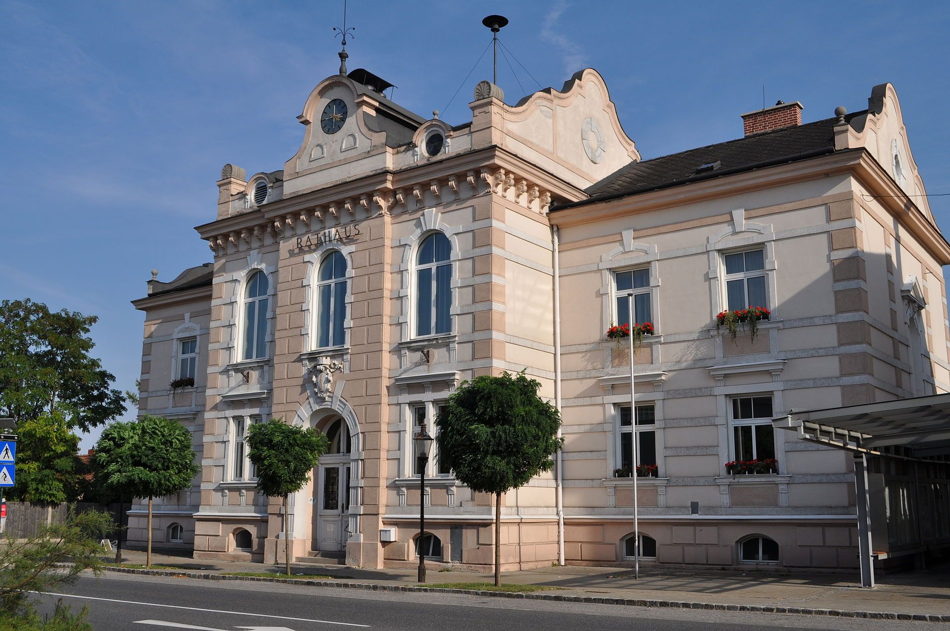 The town hall of Felixdorf, a historic building with a clock tower and ornate windows, surrounded by trees and a street in the foreground.