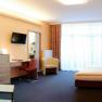 Modernly furnished hotel room with double bed, sofa, desk and large window.