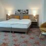 Modern double room with two beds, yellow cushions, carpet with floral pattern and a yellow armchair.