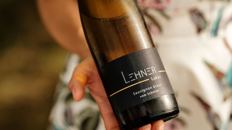 One person is holding a bottle of wine with the label 'Lehner Lukas Sauvignon blanc vom Schotter'.