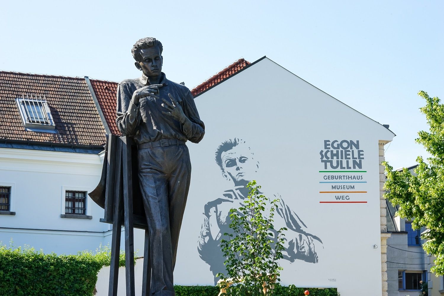 Statue of Egon Schiele in front of a building with wall painting and lettering 'Egon Schiele Tulln'.