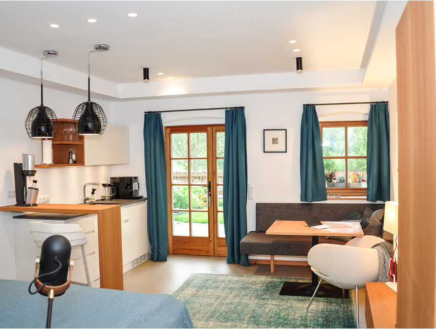 Modern studio apartment with kitchen, dining table and cozy sitting area, view of the garden through large windows.