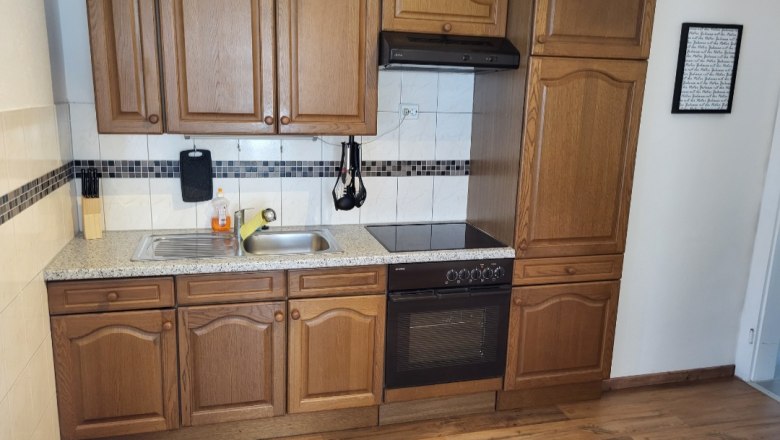 Kitchen with wooden cupboards, stove and sink.