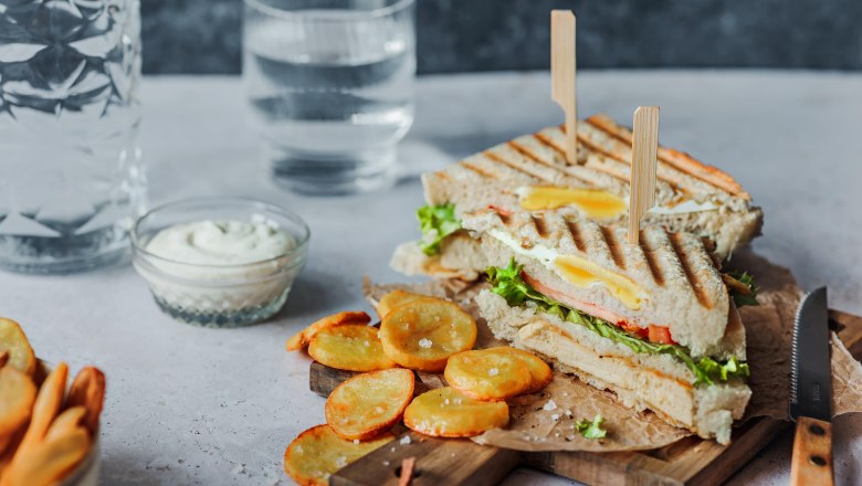 A club sandwich with chips and dip on a wooden board, with a glass of water next to it.