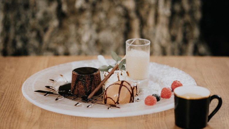 A dessert plate with chocolate cake, ice cream, berries and an espresso on a wooden table.