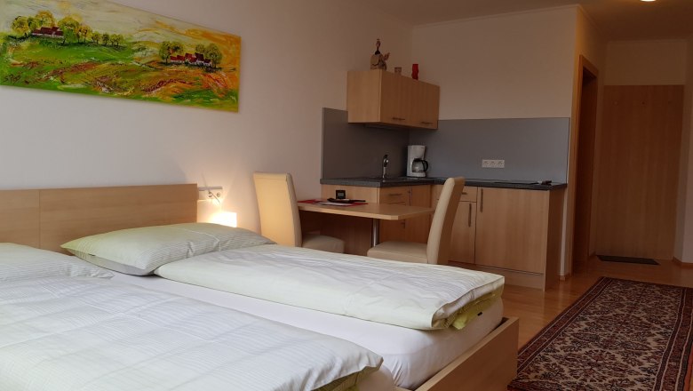 A modern room with two beds, a desk, a small kitchenette and a colorful painting on the wall.