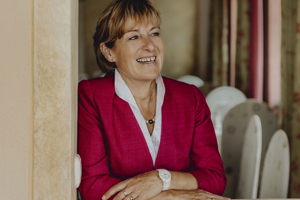 Woman in a red blazer smiles and leans against a wall.