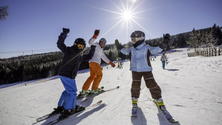 Three skiers pose happily on a sunny ski slope with a clear sky.