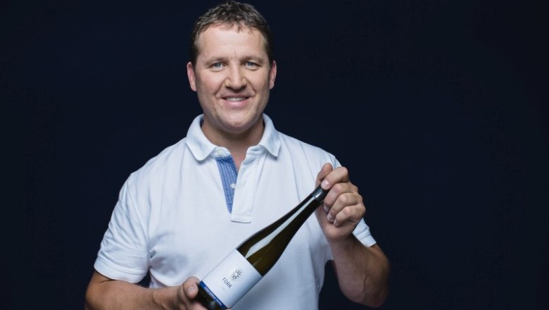 Man in white shirt holding a wine bottle with the label 'T&uuml;rk'.