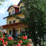Yellow hotel building with balcony, surrounded by blooming red roses and trees.