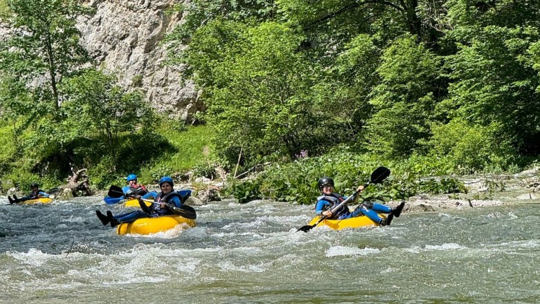 People tubing on a river in a green, wooded setting.