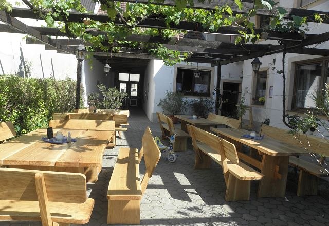 Wooden terrace with tables and benches under a pergola with vines.
