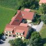 Aerial view of a large house with red roofs, surrounded by green fields and trees.