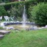 Garden with small pond and fountain, surrounded by plants and garden furniture.