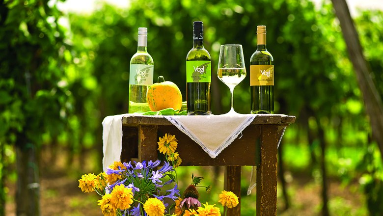 Three bottles of wine and a glass on a table in the vineyard.