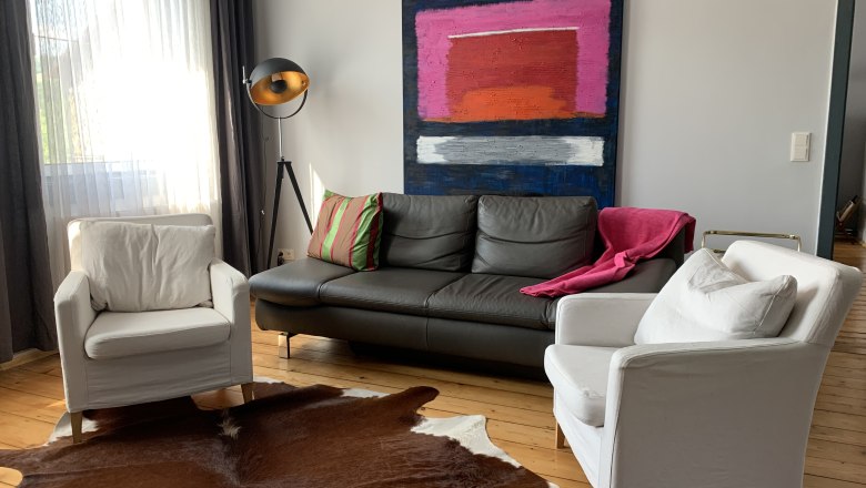 Modern living room with leather sofa, two white armchairs, floor lamp and abstract painting on the wall.