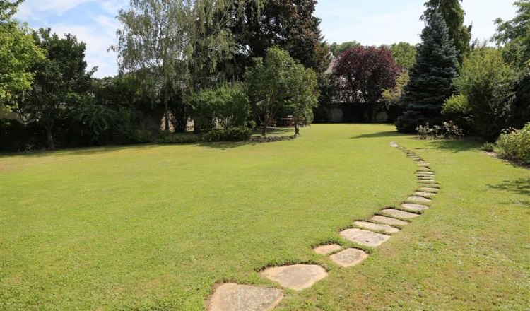 A well-kept garden with a curved stone path and trees in the background.