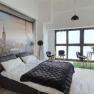 Modern bedroom with large bed, cityscape mural and seating area in front of large windows.
