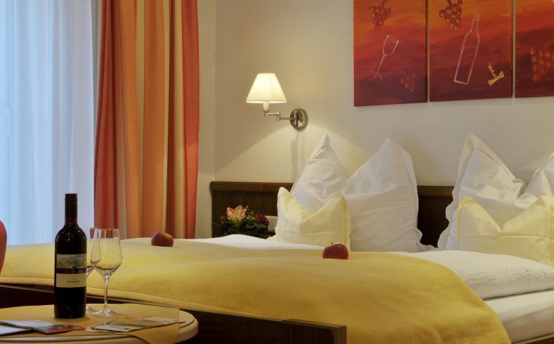 Cozy hotel room with double bed, yellow bedspread, wine bottle and glasses on the table, wall art with wine motif.