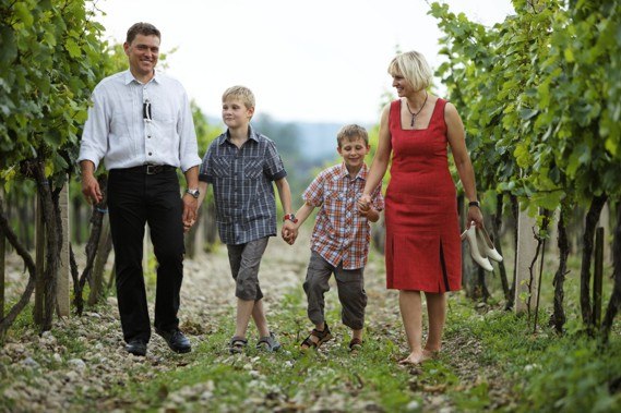 A family walks through a vineyard, consisting of a man, a woman and two boys.