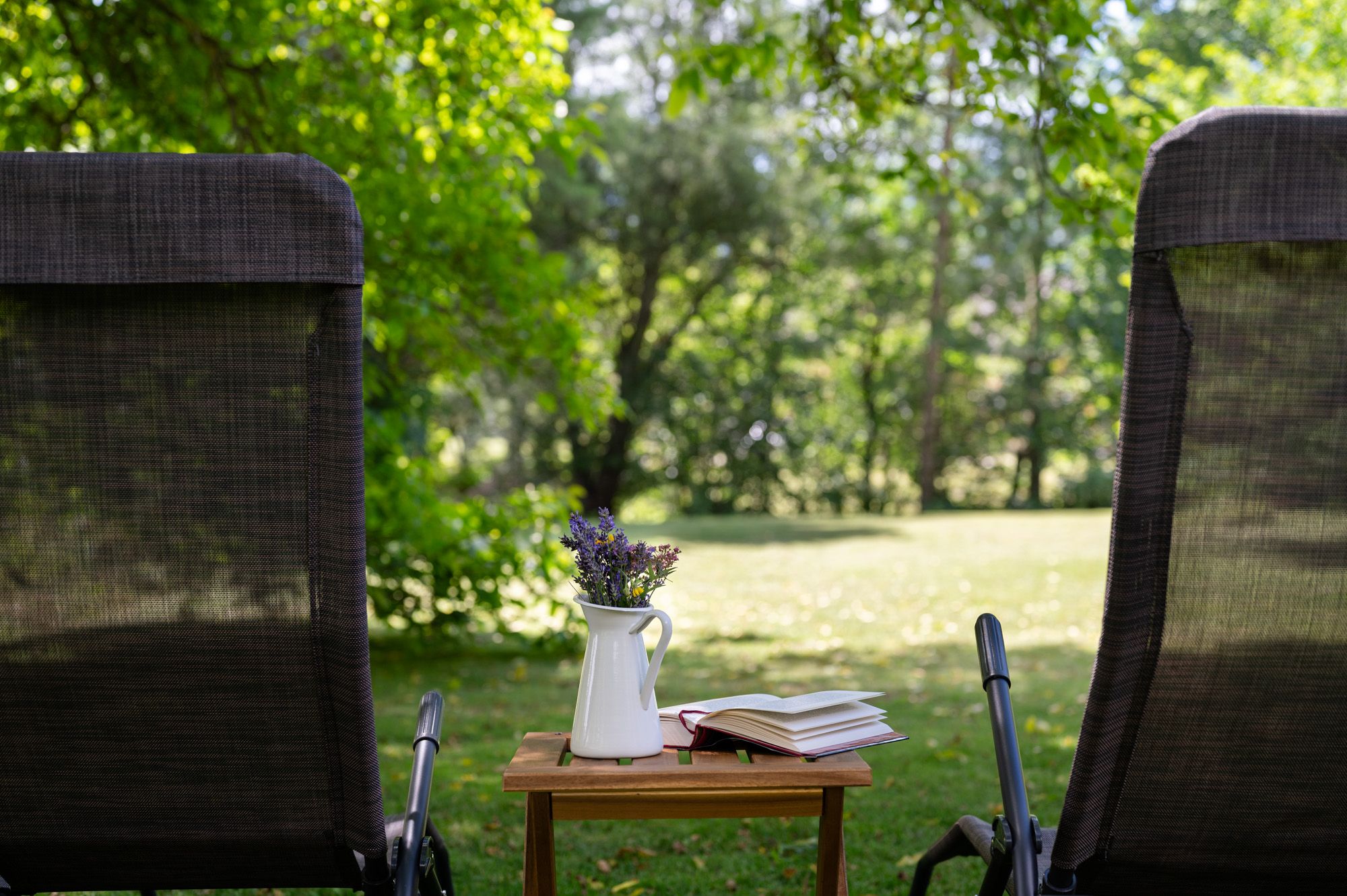 Two deckchairs in the garden with a table on which there is a vase of flowers and a book.