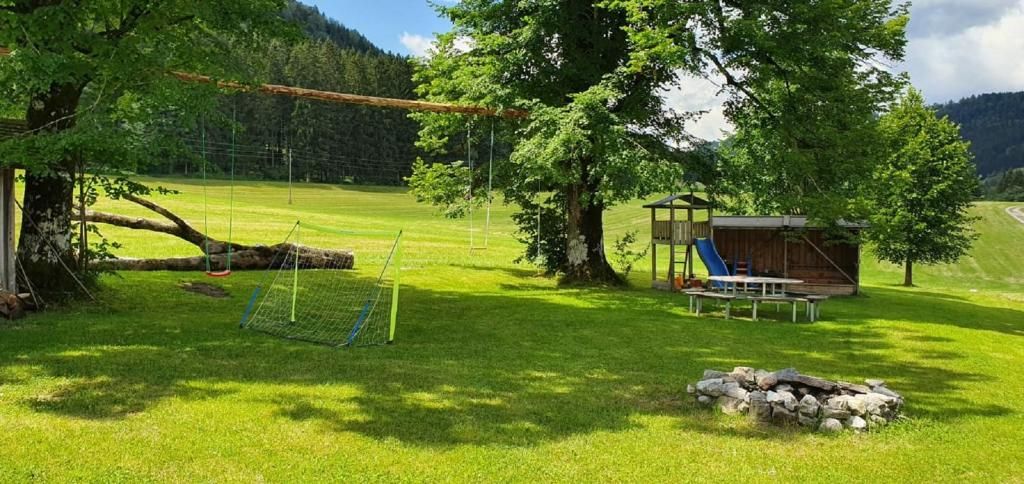 A playground on a green meadow with swings, a climbing frame, a slide, and a fire pit. Trees and hills can be seen in the background.