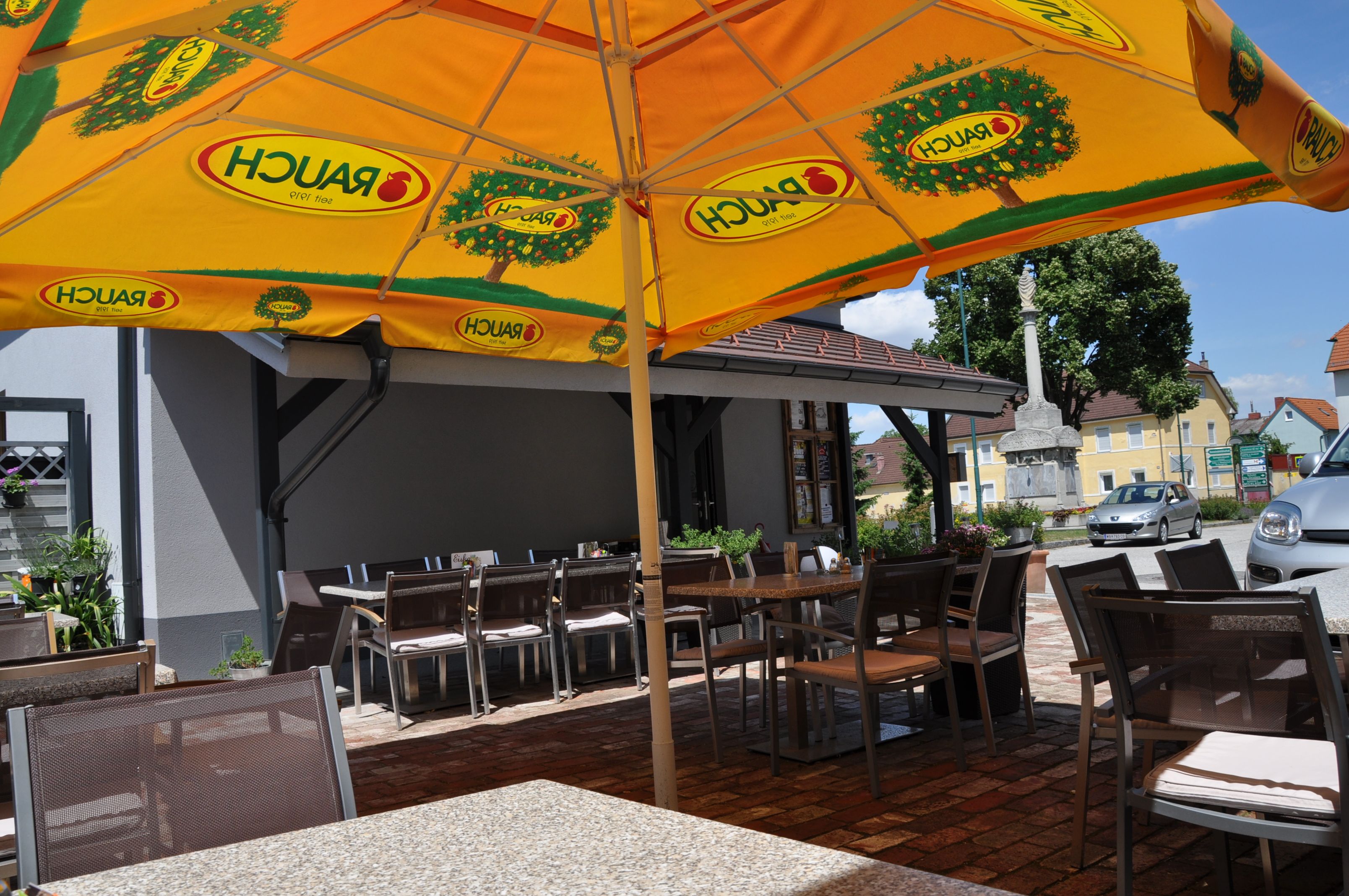 Outdoor area of a café with a yellow parasol and empty tables and chairs.