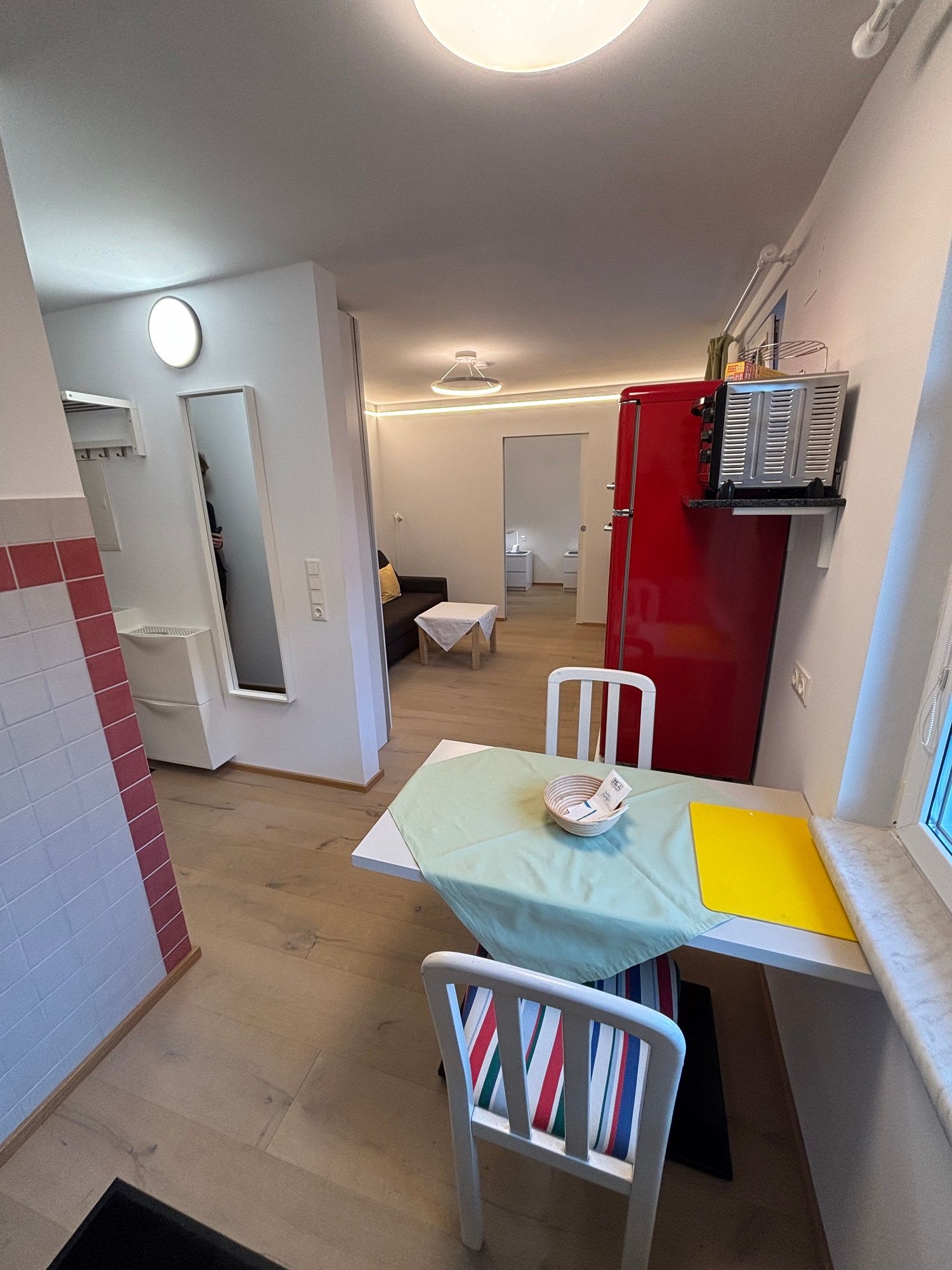 Small living room with dining table, chairs, red fridge and sofa.
