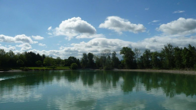 A calm lake with trees and clouds reflected in the water.