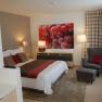 Modern bedroom with double bed, armchair and large picture of grapes on the wall.