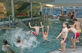 Children play and splash around in an indoor pool with water games.